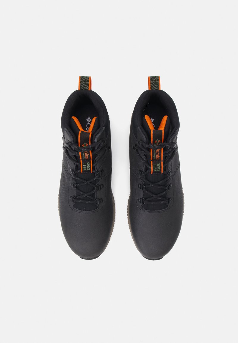 Zapatos de senderismo negros con parte superior sintética texturizada, acentos naranjas y suelas de goma. Cuentan con agujetas y un tirador para facilitar el uso.