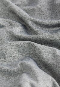 Tissu gris clair et doux avec une texture fine et lisse en tricot, présentant de légers plis qui créent des ombres et des reflets subtils.