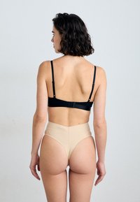 Czarny biustonosz typu bralette z regulowanymi ramiączkami, zapinany z tyłu. Beżowe majtki typu high-waisted o gładkim, bezszwowym designie.