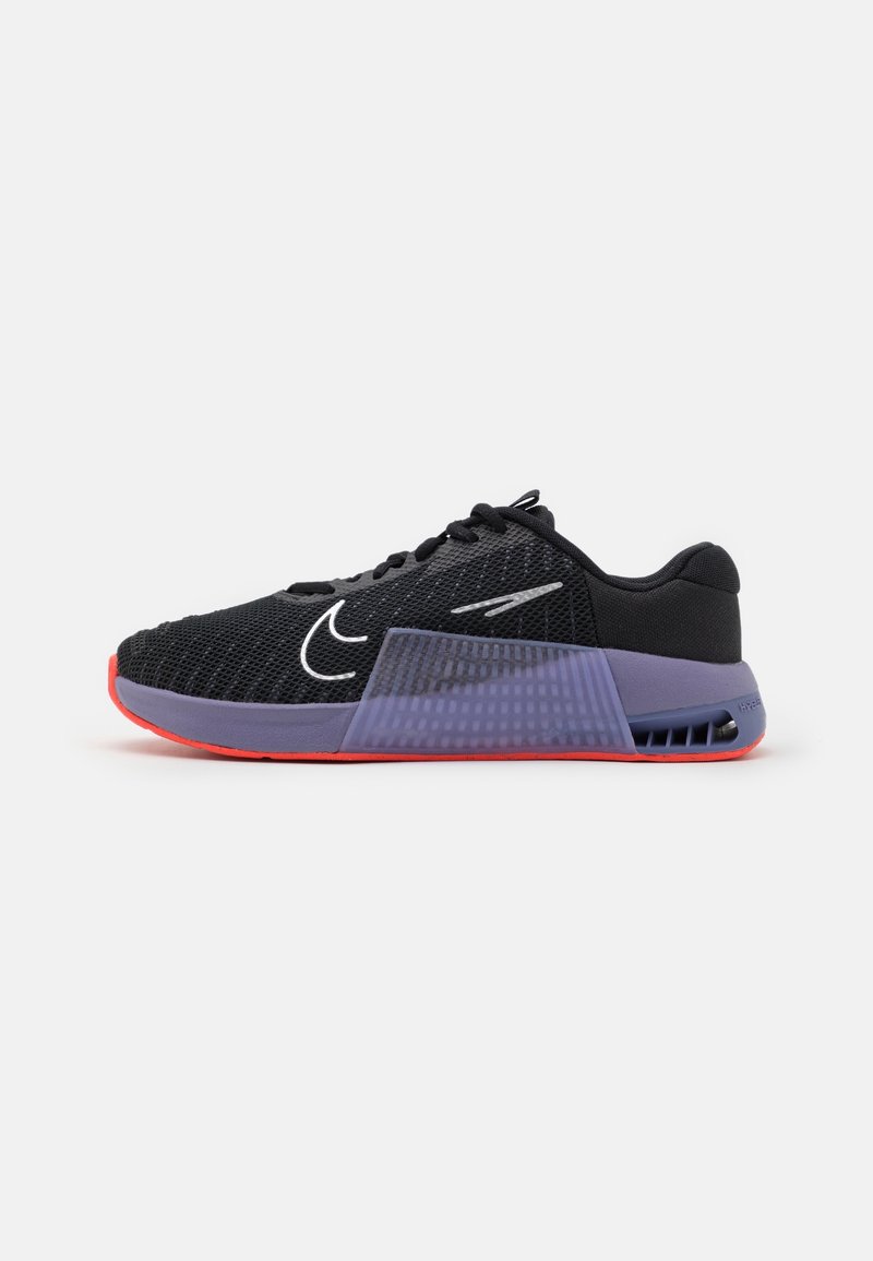Chaussure de sport noire avec dessus en mesh, midsole violet avec panneau texturé, et semelle extérieure rouge, vue de côté sur fond blanc.