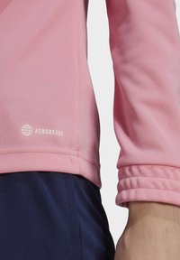 Light pink long-sleeve shirt made from textured fabric, featuring a cuffed sleeve and a white "AEROREADY" logo near the hem.