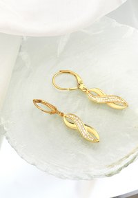 Guldtonade örhängen med vågdesign, prydda med klara kristaller. Krokupphängning, slät yta och reflekterande textur.