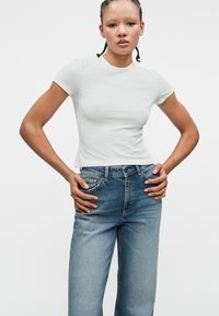 Λευκό κοντομάνικο κροπ t-shirt με στρογγυλή λαιμόκοψη, συνδυασμένο με ανοιχτό μπλε τζιν παντελόνι ψηλής μέσης με ξεθωριασμένο φινίρισμα και κλασικές τσέπες.