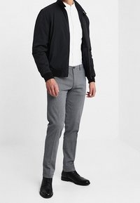 Černá bomber bunda, bílá košile, šedé kalhoty s vzorem a černé šněrovací boty. Střižené na míru; hladká látka s texturovaným vzorem.