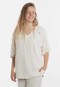 Lichtbeige linnen top met een V-hals, trekkoord en losse driekwartmouwen, gecombineerd met bijpassende broek. Subtiele textuurdetails.
