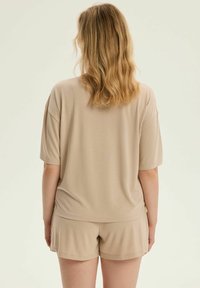 Beżowa bluzka z krótkim rękawem wykonana z miękkiego materiału, w komplecie z dopasowanymi szortami. Luźny fason, gładka faktura i minimalistyczny design.