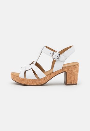 Hvid læder sandal med åben tå, korkplatform og blokhæl, justerbar ankelrem med sølvspænde samt flere stropper foran.