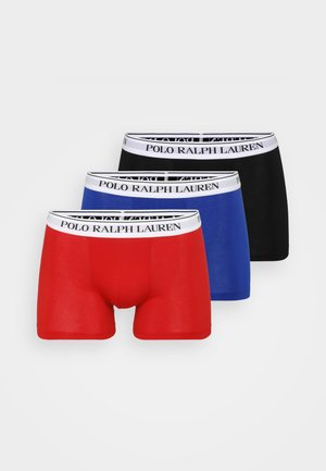 Trois paires de boxers rouge, bleu et noir avec une taille blanche portant l'inscription "POLO RALPH LAUREN". Texture de tissu lisse.