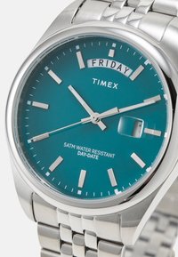Montre en acier inoxydable argenté avec un cadran teal, des index argentés et un affichage de la date. Étanche jusqu'à 5ATM, avec un bracelet à maillons.
