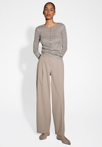 Lichtgrijze long-sleeve top met sparkles, voorzien van een ronde halslijn en knoopdetail. Beigekleurige wijde broek en bijpassende platte schoenen.