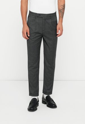 Graue karierte Hosen mit maßgeschneidertem Schnitt, mit Vordertaschen und Knopfverschluss, kombiniert mit schwarzen Loafers und weißen Socken.