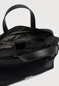 Μαύρη τσάντα ώμου με κλείσιμο με φερμουάρ, με λείο εξωτερικό, δερμάτινες χειρολαβές και εσωτερικό με επένδυση υφάσματος που διαθέτει θήκες οργάνωσης.