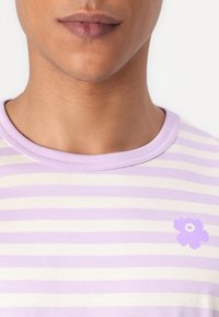 Indigo ir baltos dryžuotos marškinėlių su apvaliu kaklu, su maža violetine gėlių grafika kairėje krūtinės pusėje.