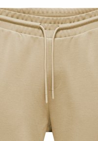 Beige Sweatpants aus strukturiertem Stoff mit einem Kordelzugbund, dezenten Nähdetails und zwei Taschen auf der Vorderseite.
