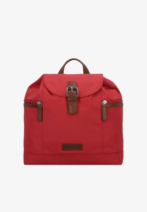 Mochila de tela roja con solapa, detalles en cuero marrón, dos cremalleras y un asa superior. Cuenta con un parche con el logo en la parte frontal.