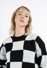 Schwarzer und weißer karierter Pullover mit einer strukturierten, flauschigen Oberfläche, rundem Ausschnitt und überschnittenen Schultern, der große Blockmuster aufweist.