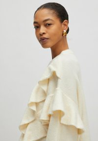 Ivory truien met gelaagde ruffles, gemaakt van zacht textiel. Kenmerkt zich door een ronde hals en lange mouwen. Eenvoudige, elegante uitstraling.