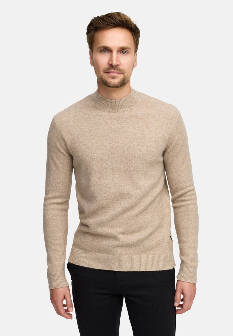 Maglione lavorato a maglia beige chiaro con scollo rotondo a costine e maniche lunghe. Caratterizzato da una texture liscia e una forma aderente. Pantaloni neri visibili.