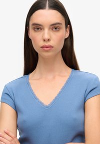 Camiseta de color azul claro de canalé con mangas cortas y escote en V, adornada con un delicado ribete de encaje en el cuello. Textura suave.