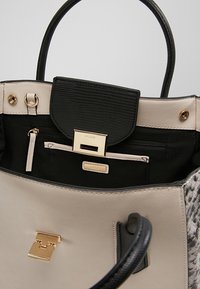 Grå och svart handväska med texturerad yta, guldaccessoarer, en dragkedjefack och en täckt ficka inuti. Mjukt lädermaterial.