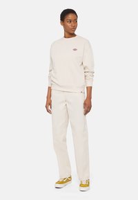 Felpa beige a collo rotondo con logo ricamato, abbinata a pantaloni crema e sneakers gialle. Linea rilassata con polsini e vita a coste.