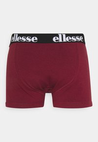 Bordeauxfarbene Boxer-Shorts aus weichem Material mit einem schwarzen Elastikbund, der mit dem weißen "ellesse"-Logo bedruckt ist. Standardgröße mit genähten Nähten.