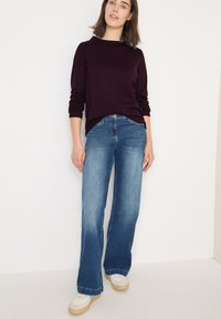 Tmavě fialový dlouhý rukáv tričko spárované se světle modrými kalhotami širokého střihu a bílými teniskami. Hladký materiál, pohodlný střih a viditelné detaily šití.