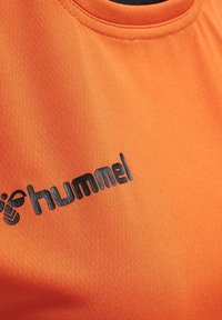 Camiseta deportiva naranja con una tela texturizada. Presenta un logotipo negro de "hummel" impreso en el pecho. Cuello redondo.
