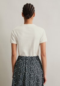 Krämfärgad kortärmad skjorta med rund hals, bärs tillsammans med en svart mönstrad kjol som har olika små former och ikoner.