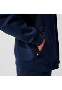 Hoodie bleu marine avec un panneau texturé, poche zippée et poignets côtelés. Fabriqué à partir d'un mélange de matériaux lisses et respirants.