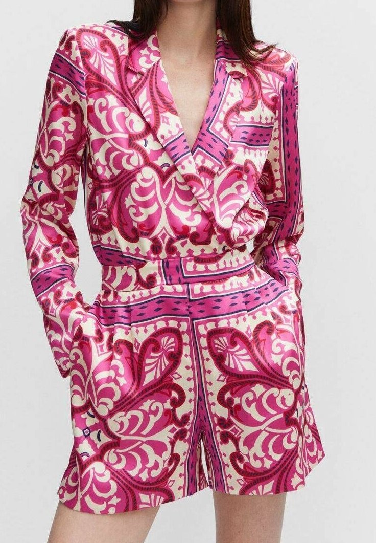 Femme portant un blazer à manches longues rose et blanc à motifs et un short taille haute assorti, les mains dans les poches.