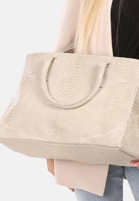 Sac fourre-tout en cuir de serpent beige avec surface texturée, deux poignées et un design spacieux. Panneau inférieur lisse et légère brillance.
