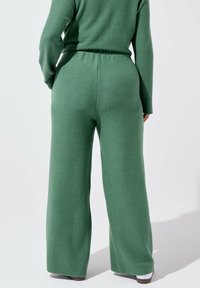 Pantalons larges verts en tissu doux et texturé. Taille élastique pour le confort. Coutures minimales et pas de matériel visible.