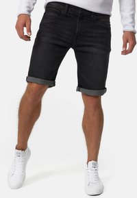 Shorts en denim noir avec ourlets roulés, présentant un design classique à cinq poches. Associés à des baskets montantes blanches. Look simple et épuré.