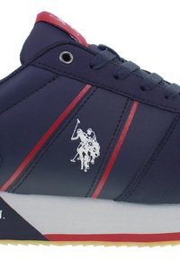 Sneaker blu con strisce rosse e lacci rotondi. Presenta una tomaia testurizzata, suola in gomma e un logo di un giocatore di polo argentato sul lato.