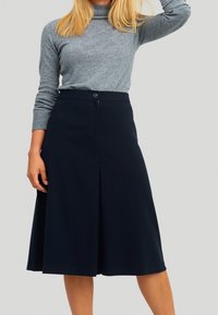Marineblaues A-Linien-Rock mit einer Faltenlegung an der Vorderseite und Knopfverschluss, kombiniert mit einem grauen Langarmpullover. Sanfte Stofftextur.