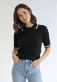 Czarna dzianinowa koszulka polo z teksturowanym wzorem warkocza, z kołnierzem z białym wykończeniem i krótkimi rękawami z dopasowanymi paskami.