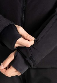 Schwarze, figurbetonte Jacke mit Reißverschluss, langen Ärmeln mit Daumenlöchern und Klettverschlussverstellungen an den Bündchen. Glattes, leichtes Material.