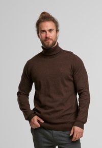 Brauner Rollkragenpullover aus weichem Strickmaterial, mit langen Ärmeln und taillierter Passform. Dezentes Logo-Detail auf der Brust.