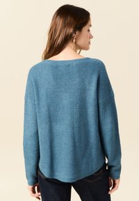 Een ruime teal trui met een textuur breiwerk, voorzien van een brede halslijn en verlaagde schouders, eindigend bij de heupen met een gebogen zoom.