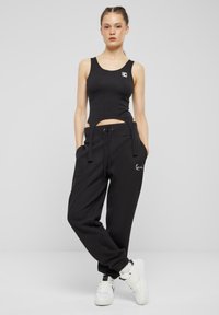 Svart kort tanktopp parret med løse svarte joggebukser med lommer og snøring. Hvide logo detaljer på begge deler. Hvite sneakers.