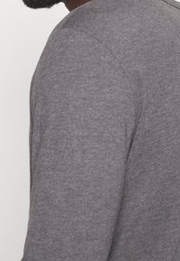 Dunkelgraues Langarmshirt aus einem weichen, strukturierten Stoff, mit einem runden Ausschnitt und schlanker Passform.