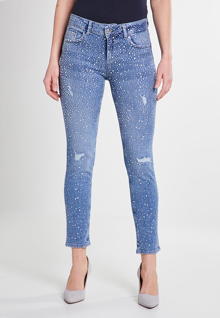 Jeans skinny blu con un design strappato e decorazioni simili a perle, cinque tasche e chiusura con bottone.