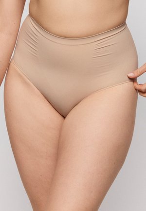 Close-up van een persoon die naadloze beige shapewear slips met een hoge taille draagt, met één hand die de heupband aan de zijkant verstel.