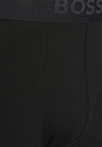 Black cotton boxer shorts with an elastic waistband featuring a subtle logo. Smooth texture with a fitted design and minimal stitching details.