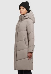 Beige padded coat with a hood, diagonal quilted design, front zipper, and two side pockets. Worn with a black knitted beanie.
