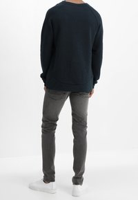 Sudadera azul marino oscuro con mangas raglán, con un dobladillo curvo, combinada con jeans ajustados de color gris claro y zapatillas blancas.