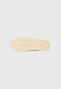 Semelle d'une sneaker en caoutchouc beige clair, dotée d'un motif en zigzag texturé et de détails de grip circulaires pour une meilleure adhérence.