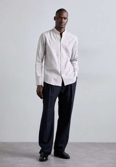 Light gray button-up shirt with a mandarin collar, paired with dark navy trousers and glossy black shoes, standing against a neutral background.