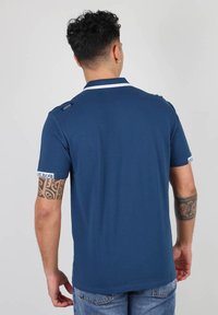 Polo shirt bleu marine avec un col et des accents de poignets blancs. Doté d'un petit logo sur l'épaule et d'une texture de tissu lisse.